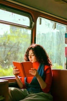 Young woman reading a book while traveling on a bus, bathed in natural light.