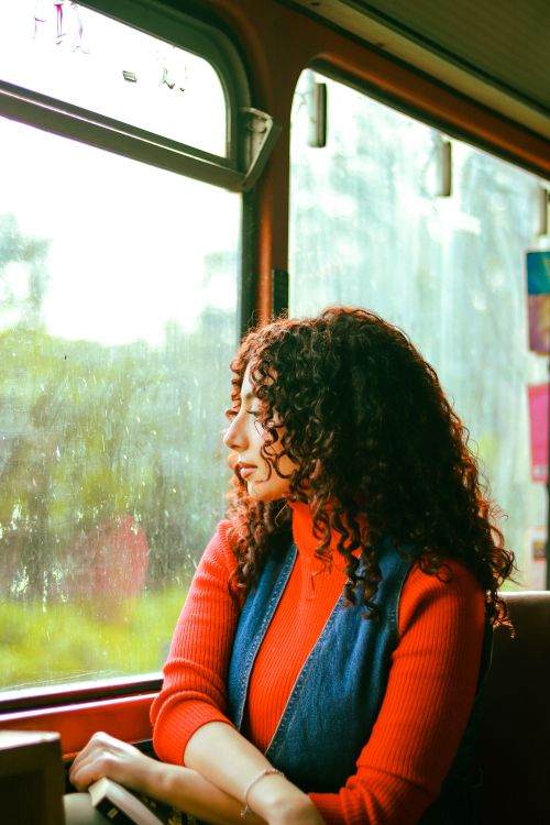 Free A woman with curly hair looks out the window of a city bus during the day. Public transportation scene. Stock Photo