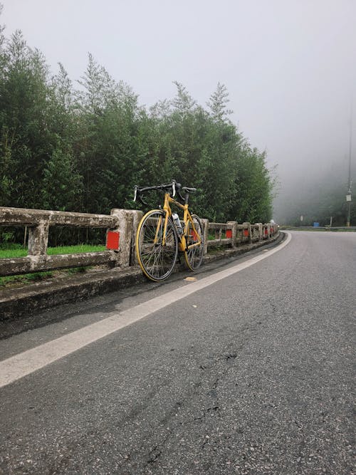 A yellow bicycle leaning against a wooden fence on a foggy road