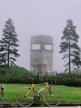 A yellow road bike parked near a foggy abandoned tower in a rural landscape.