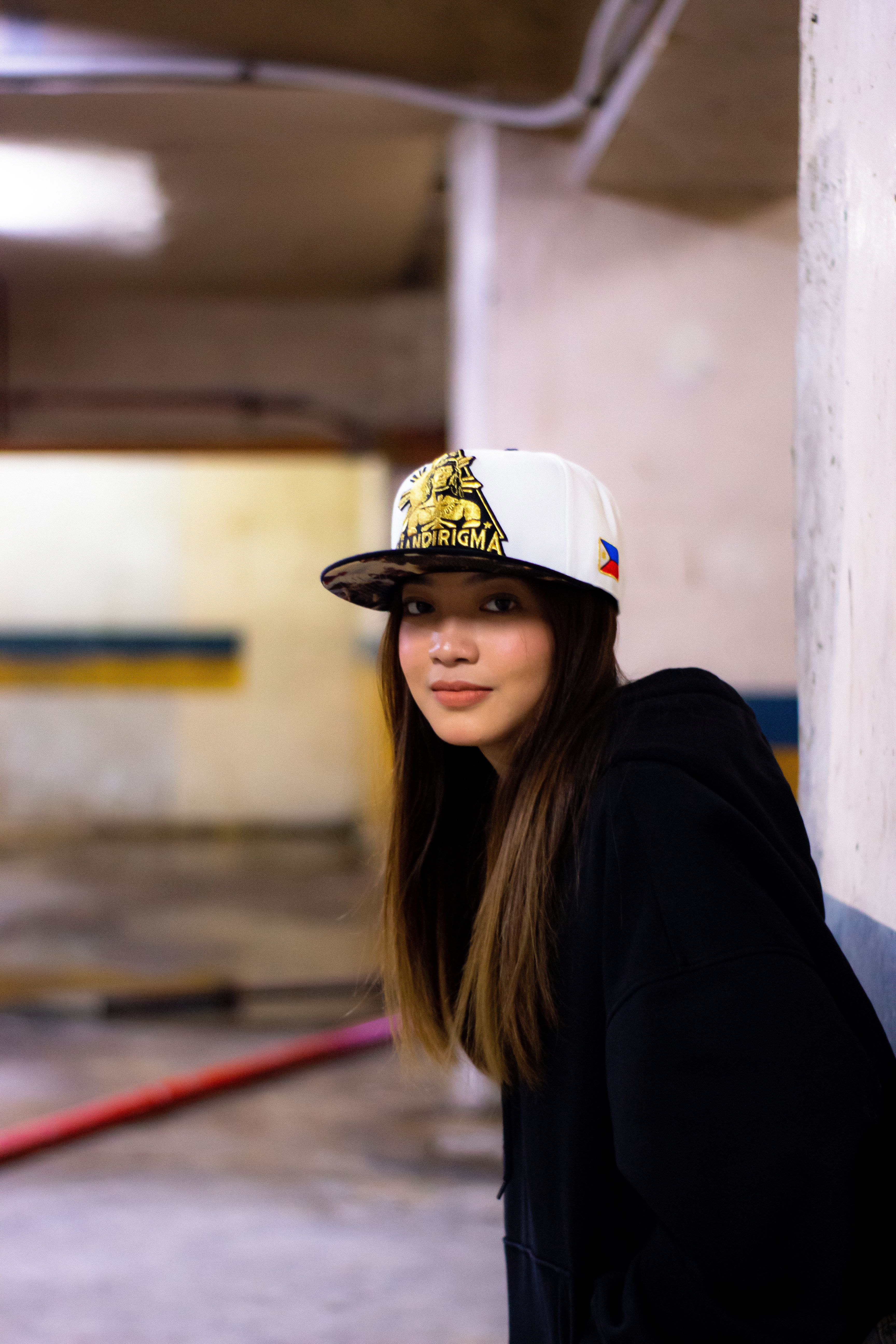 Portrait of a woman in a cap posing confidently in an urban parking garage setting.