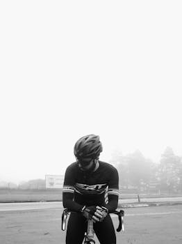 A cyclist dressed in sportswear and helmet sits on a bike in foggy weather. Black and white style.