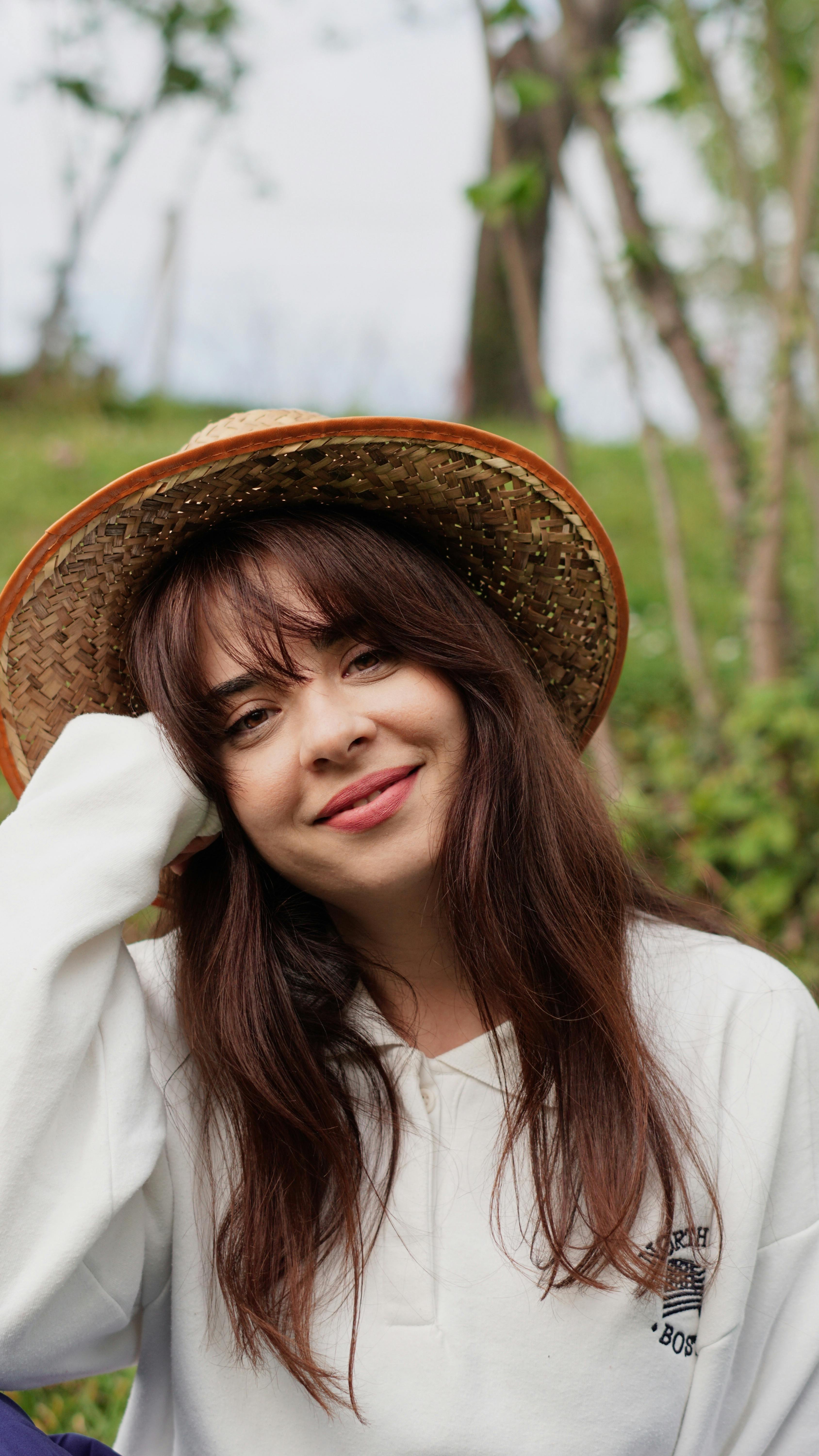 Charming portrait of a woman smiling outdoors, wearing a stylish hat and casual attire.