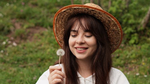 Free A woman in a straw hat is smiling while holding a dandelion Stock Photo