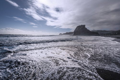 A beach with waves and rocks in the background