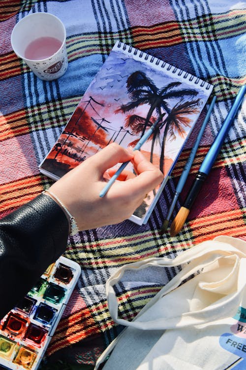 Free A person painting on a picnic blanket with watercolor paints Stock Photo