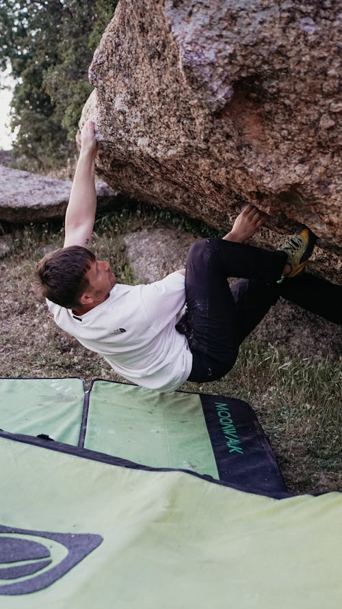 A man climbing on a rock with a green bag