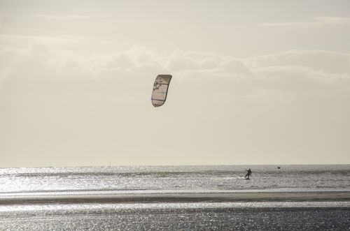 Free Silhouetted kite surfer enjoying sports on ocean waves during a serene sunset. Stock Photo