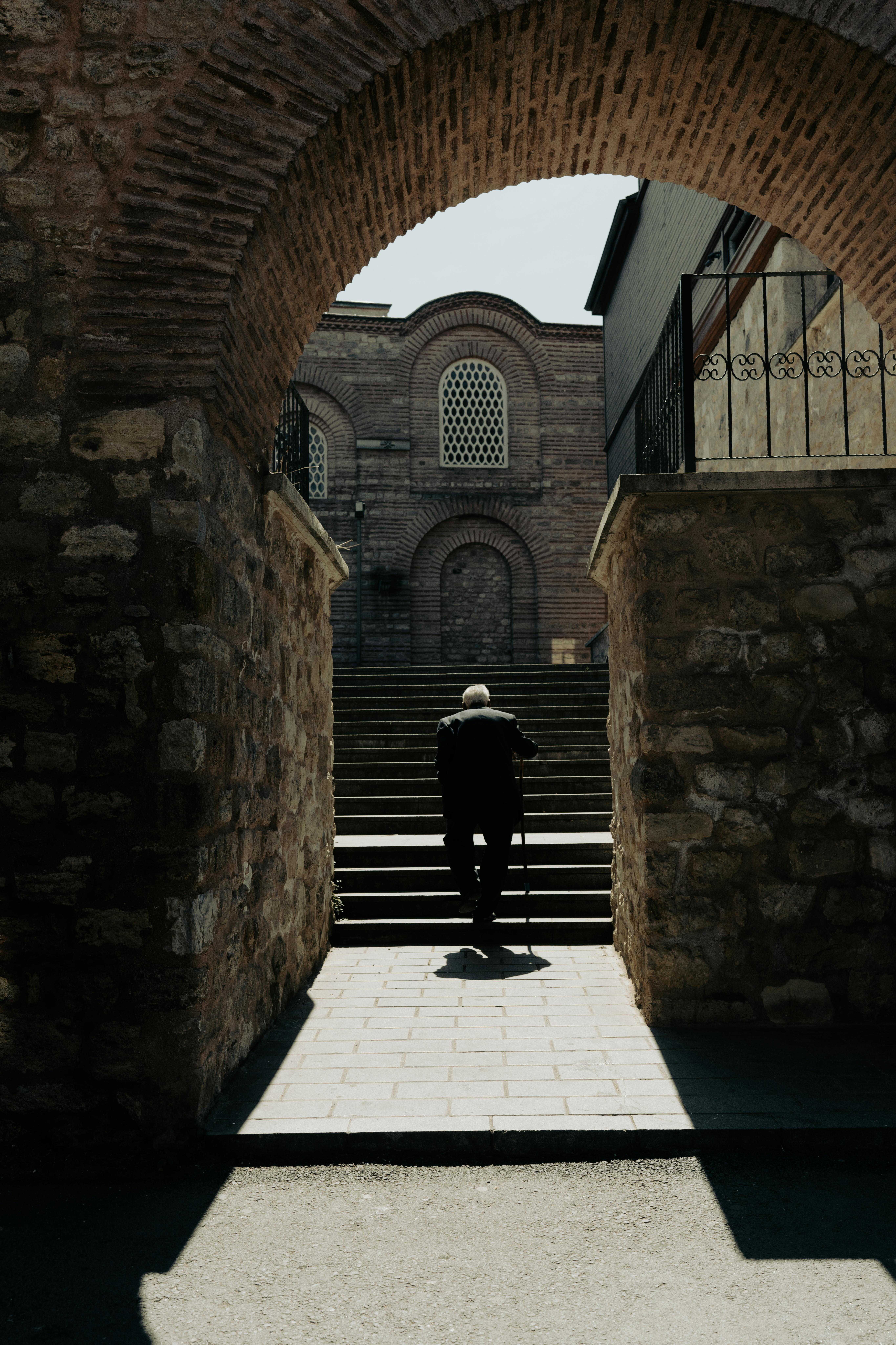 A senior man walks up historic stone stairs in an urban archway setting.