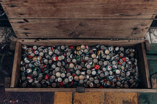 A top view of a wooden chest filled with assorted vintage beer bottle caps.