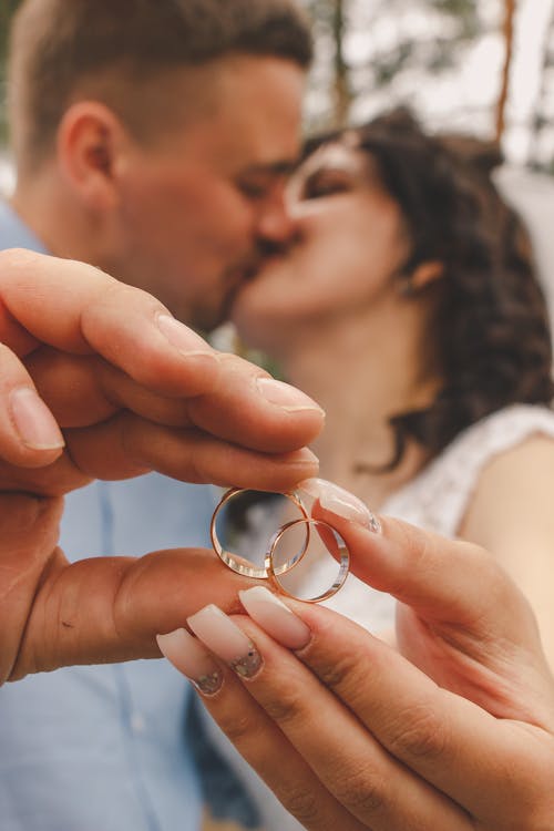 A man and woman kissing while holding wedding rings