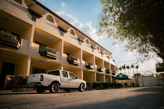 Sunlit hotel facade with a white pickup truck parked outside, showcasing modern architecture.
