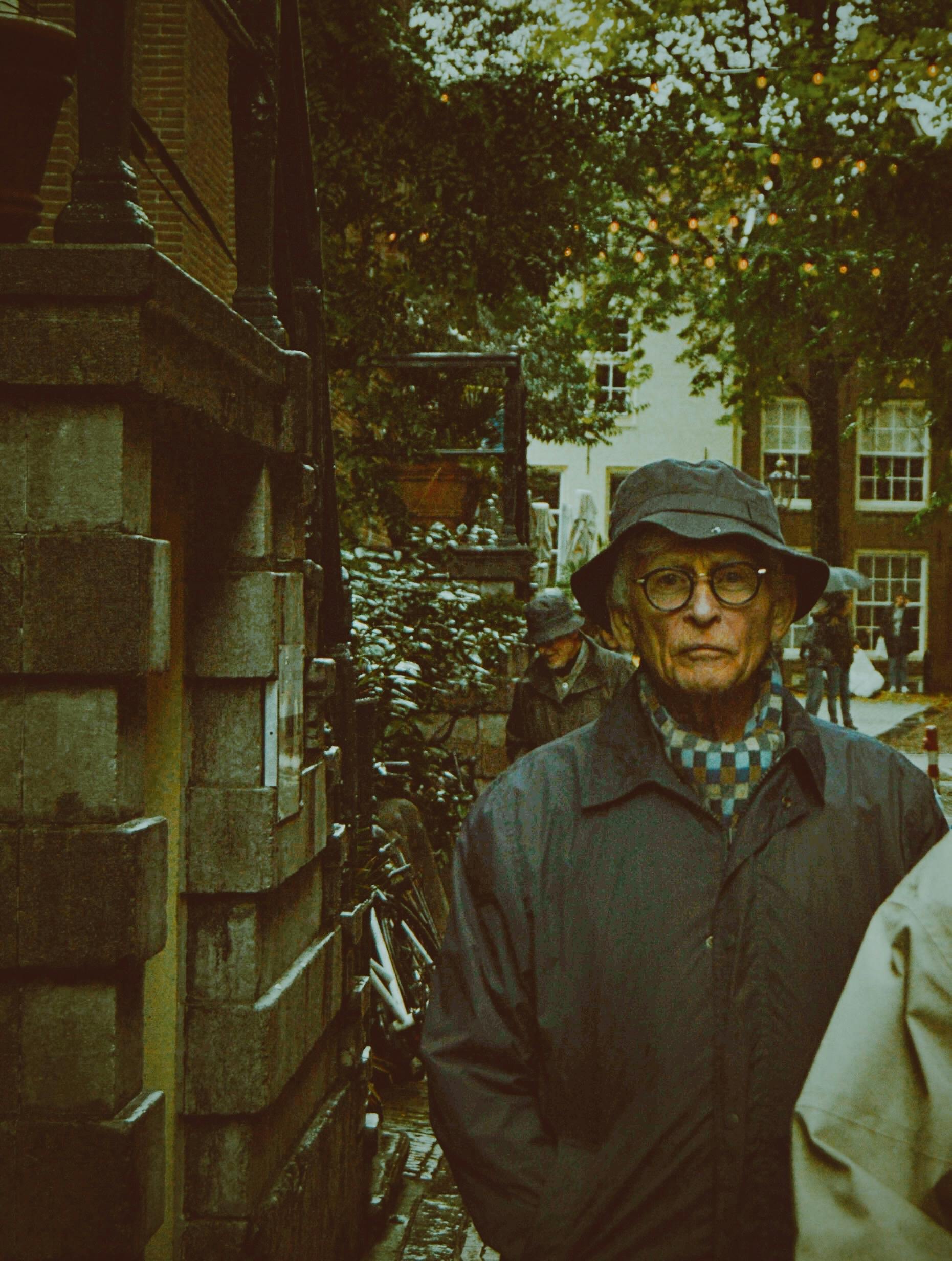 Elderly man with glasses and hat walks in a moody urban street, capturing autumn's essence.