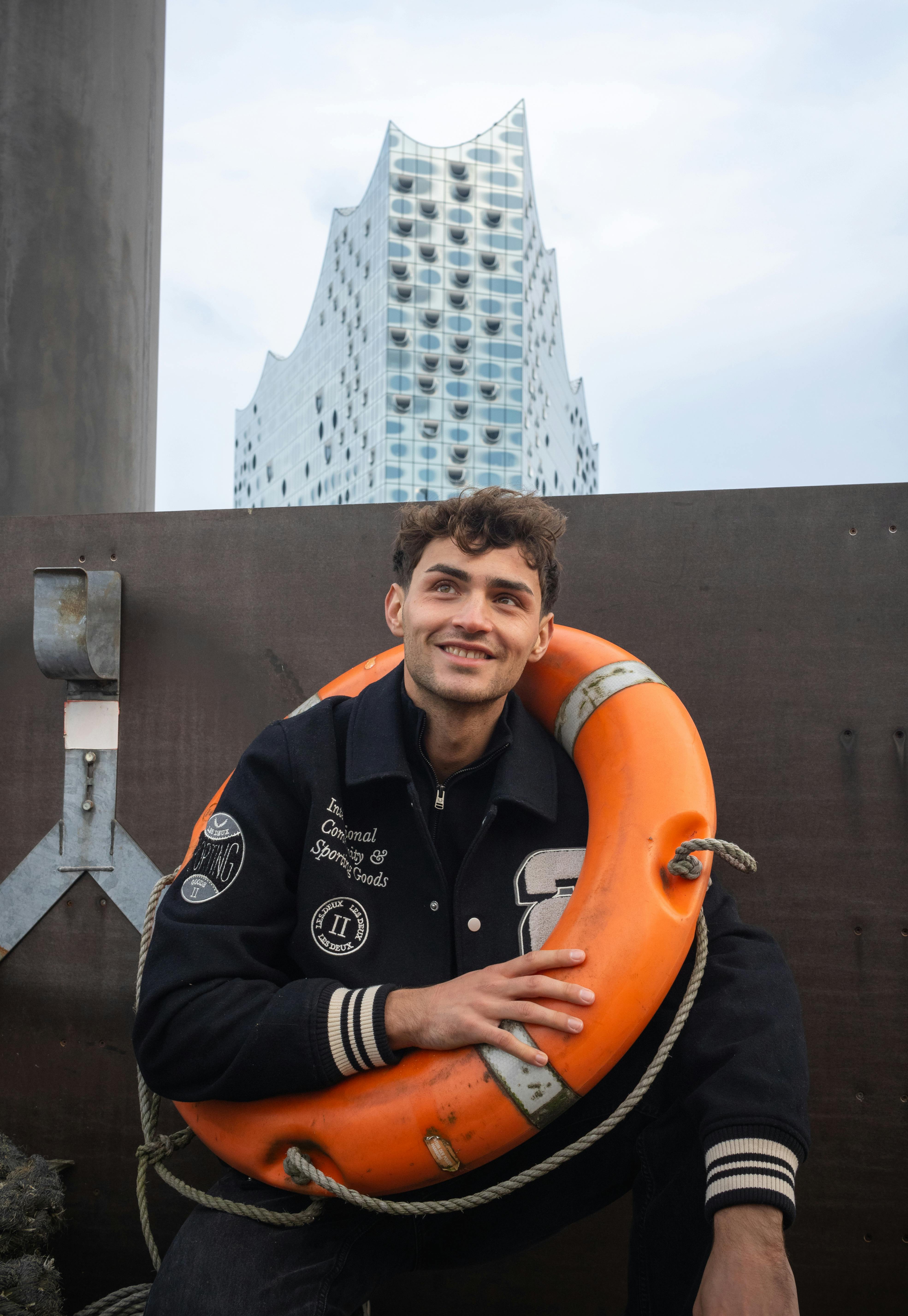 Happy man wearing a black jacket with a lifebuoy in Hamburg, Elbphilharmonie in the background.
