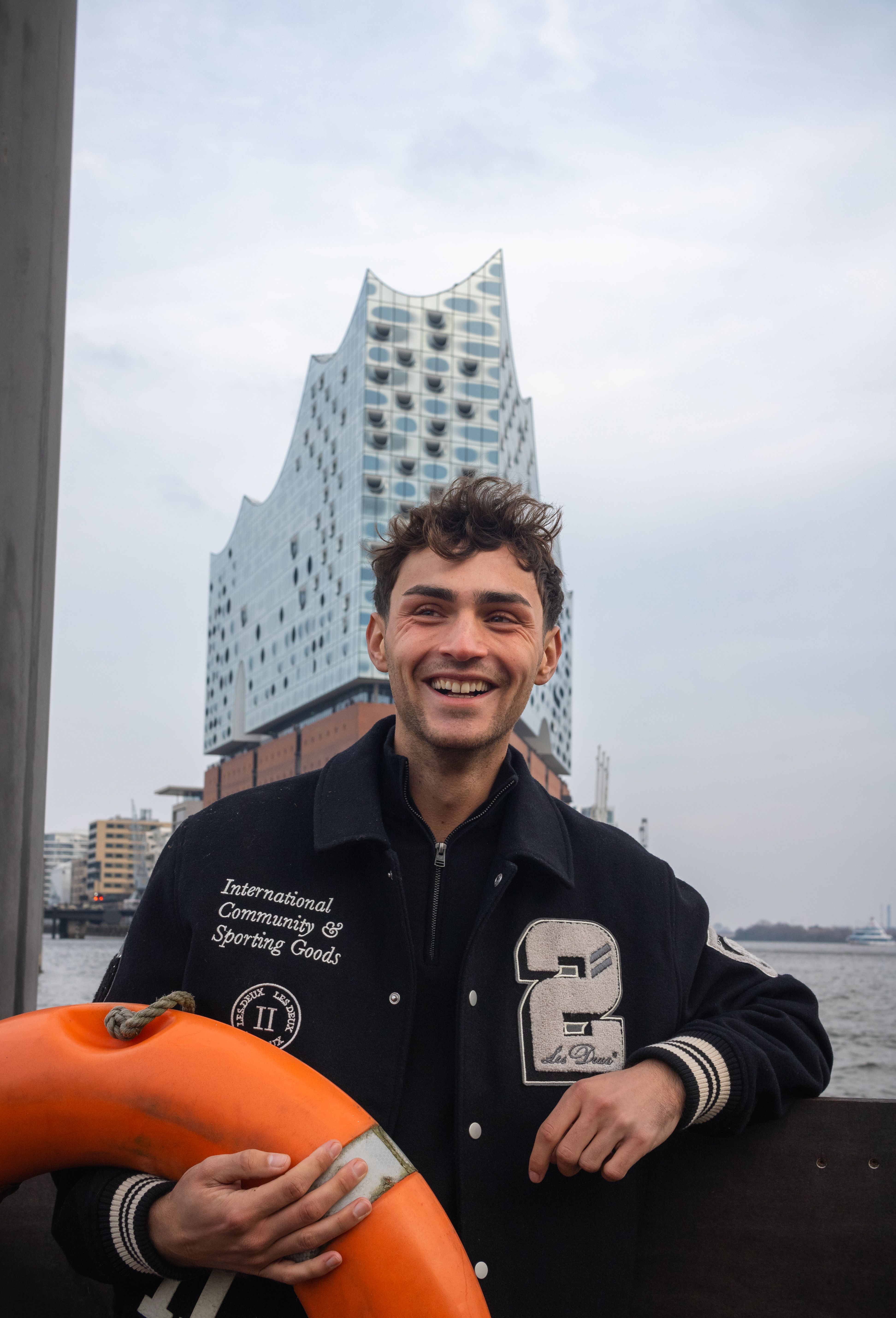 Cheerful man in Hamburg with the iconic Elbphilharmonie in the background, a perfect blend of fashion and architecture.