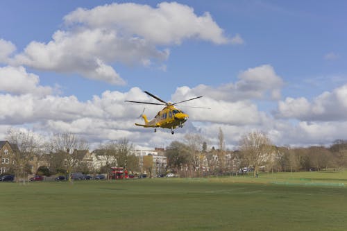 A yellow helicopter flying over a grassy field