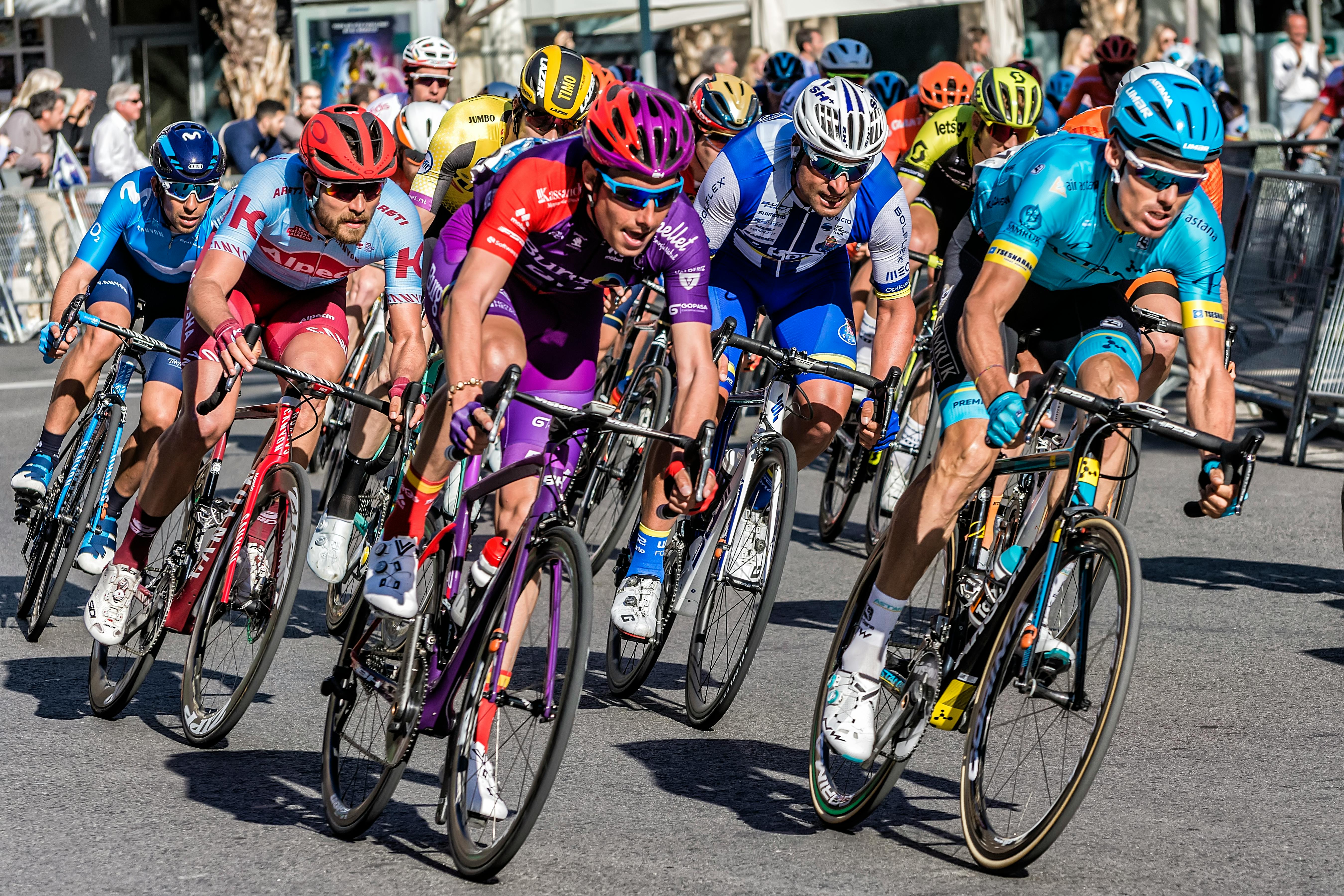 Competitive cyclists in vibrant gear race through Alicante streets, showcasing speed and athleticism.