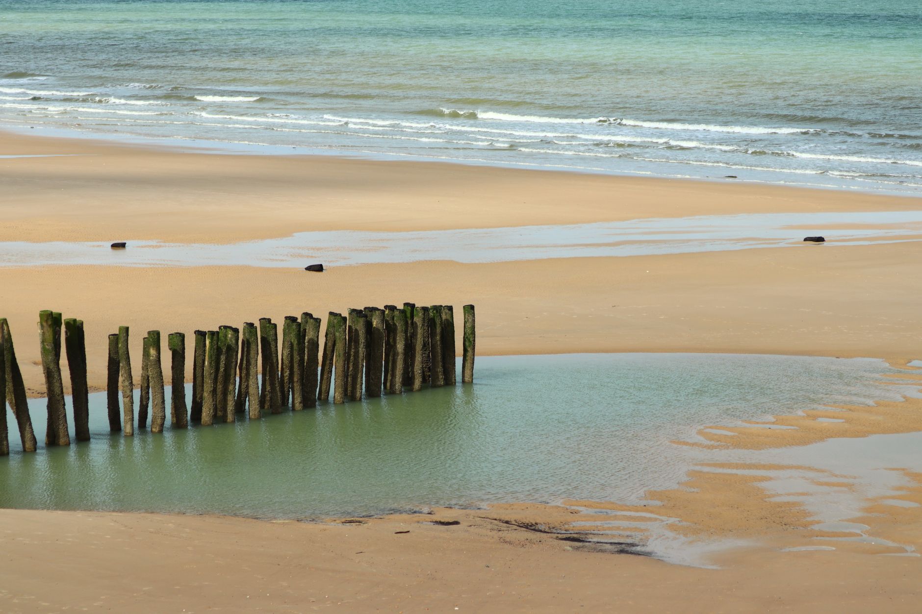 A peaceful beach with wooden groynes and waves in Wissant, France.