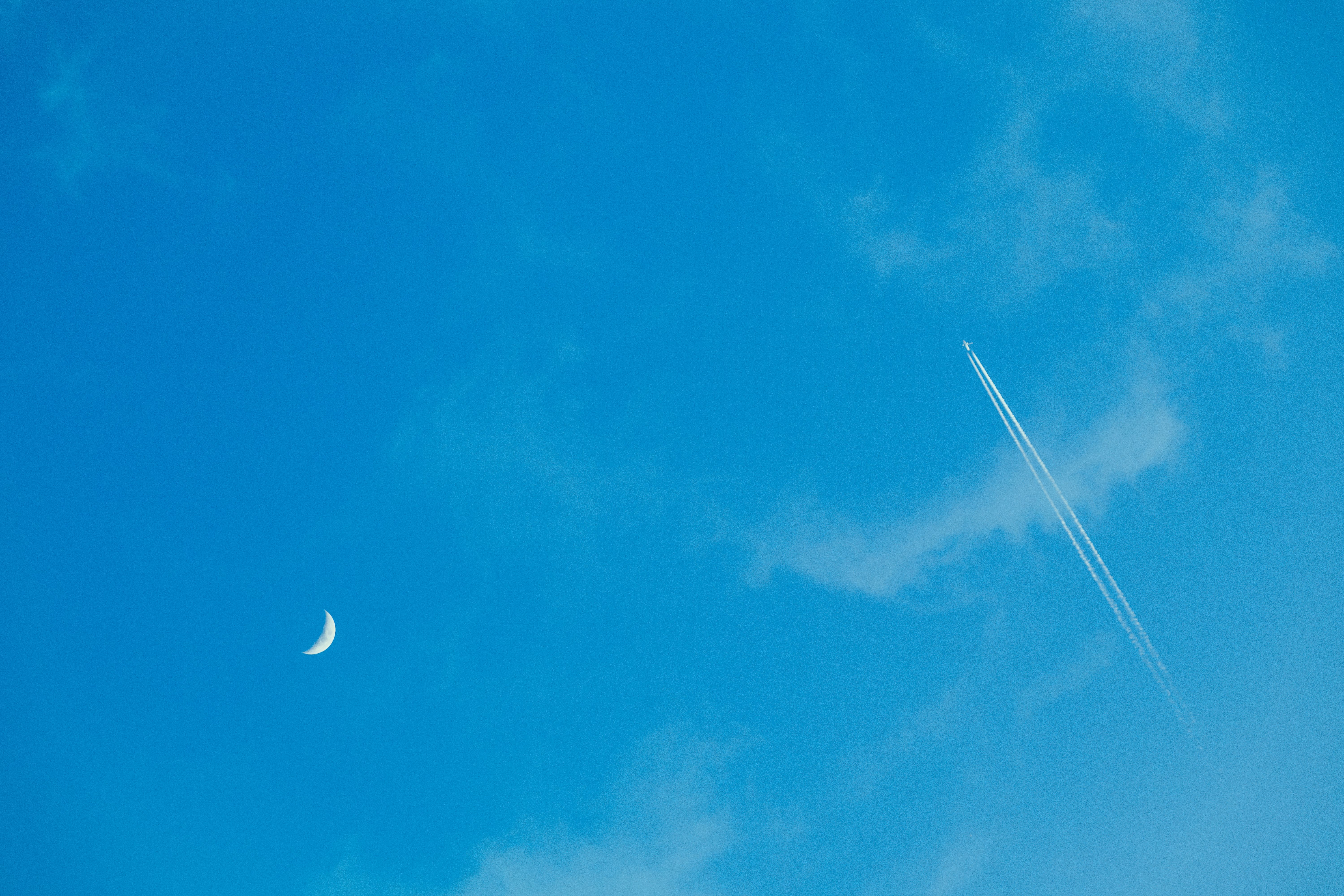 A crescent moon and jet airplane with contrails in a clear blue sky. - Zaragoza