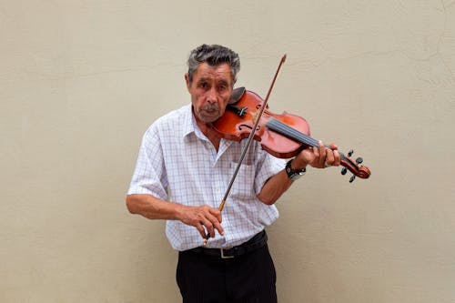 An older man playing the violin in front of a wall