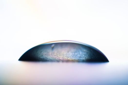 Captivating close-up of a water droplet creating a colorful reflection on a smooth surface.