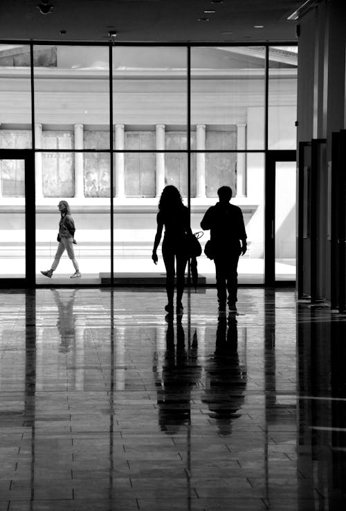 Free Silhouette of two people walking through a large building Stock Photo