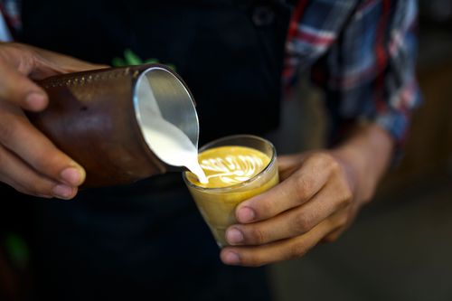 Free Barista expertly pouring steamed milk to create latte art in a coffee shop setting. Stock Photo