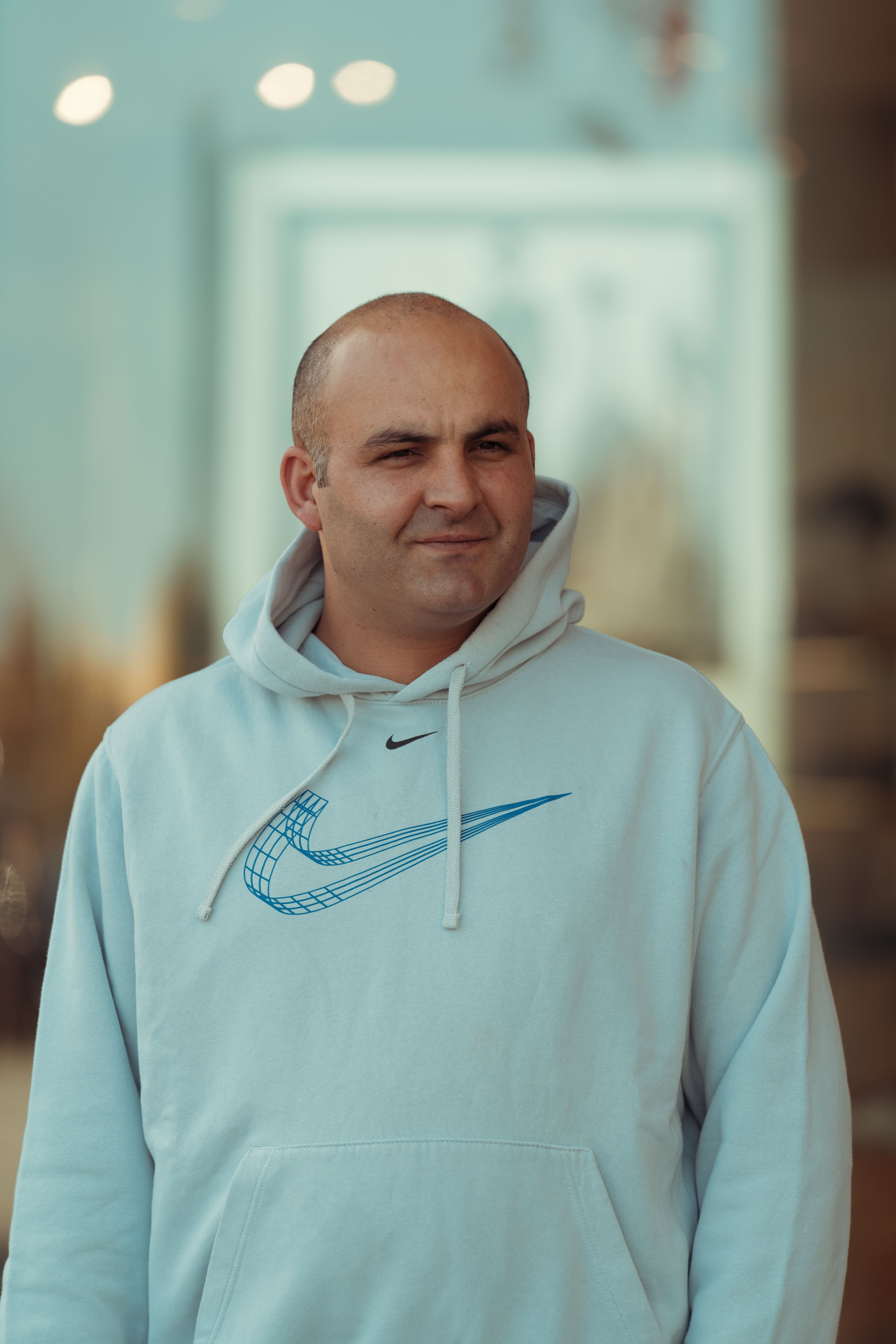 Portrait of a bald man wearing a hoodie, standing casually outdoors with blurred background.