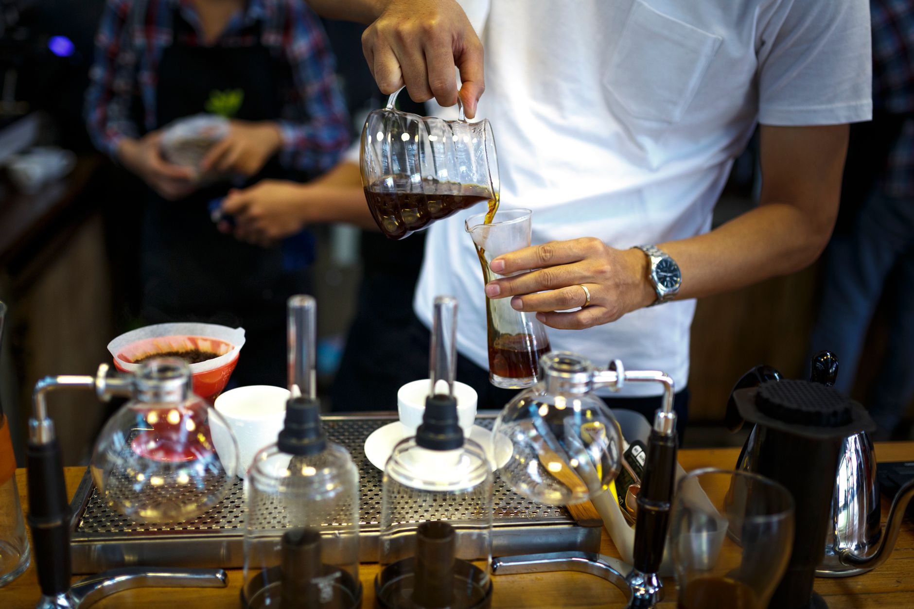 A barista carefully pouring brewed coffee into a clear glass in a coffee shop.