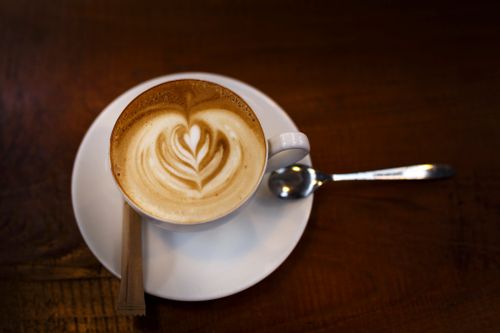 Free Close-up of a beautifully crafted latte with artistic foam design on a wooden table. Stock Photo