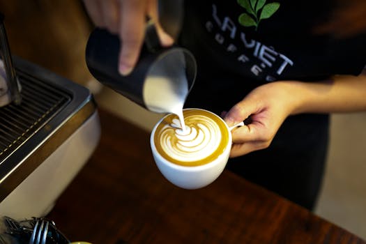 Barista creating intricate latte art on a frothy cappuccino in a cozy cafe setting.