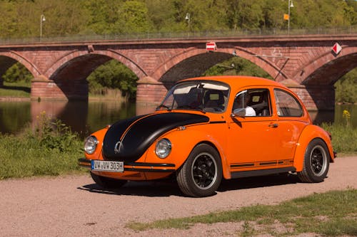 VW Käfer in Orange in der Lanschaft fahrend im Hintergrund eine Brücke