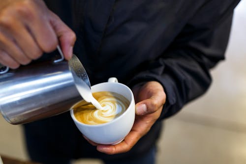 Person Pouring Milk on White Coffee