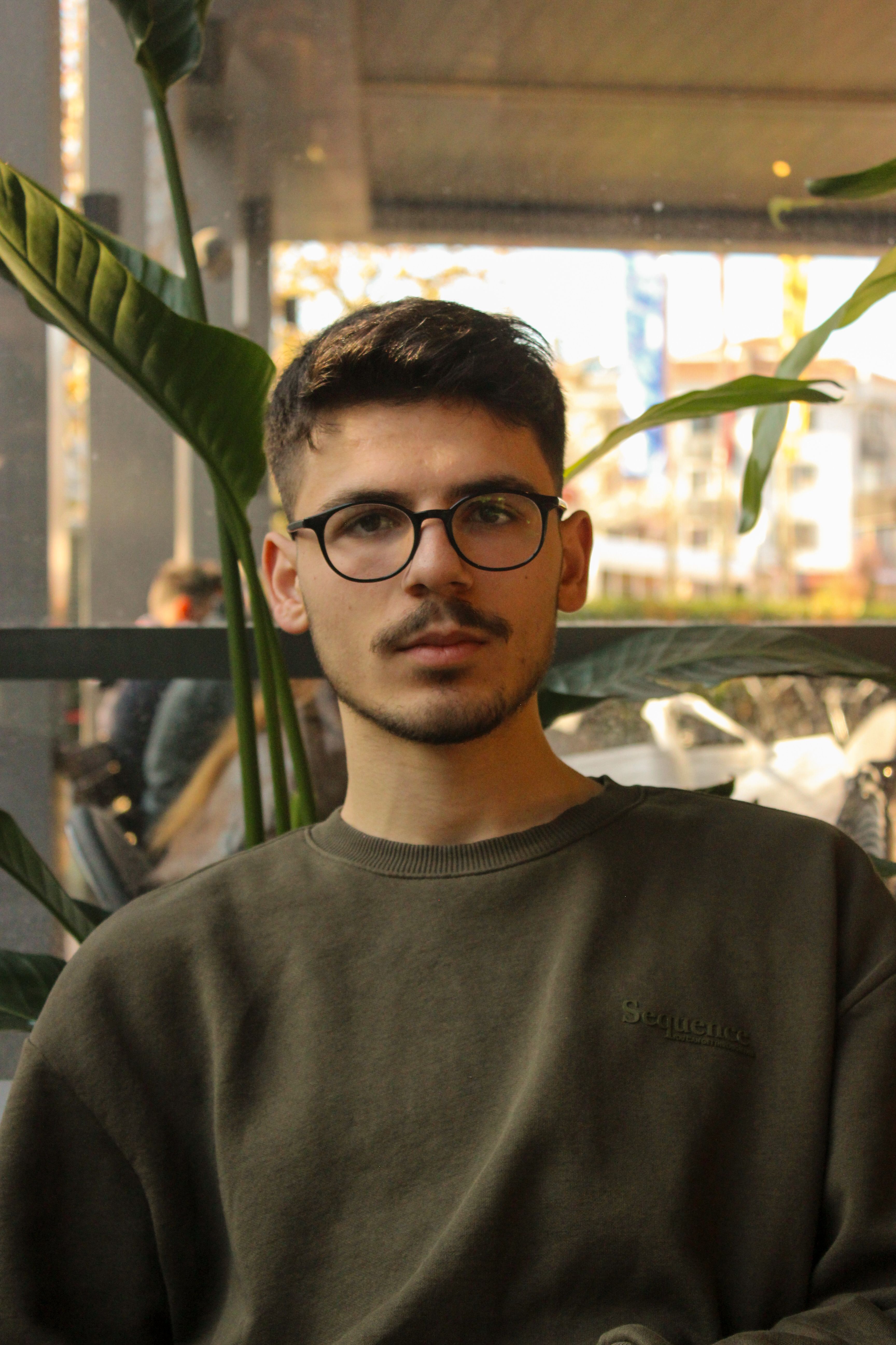 A stylish portrait of a young man with glasses and moustache sitting indoors