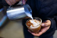 咖啡师将蒸牛奶倒入玻璃咖啡杯，创作出复杂的拿铁艺术特写