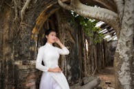 一位身穿白色奥黛的美丽女子，在藤蔓覆盖的古老建筑前优雅地摆出姿势