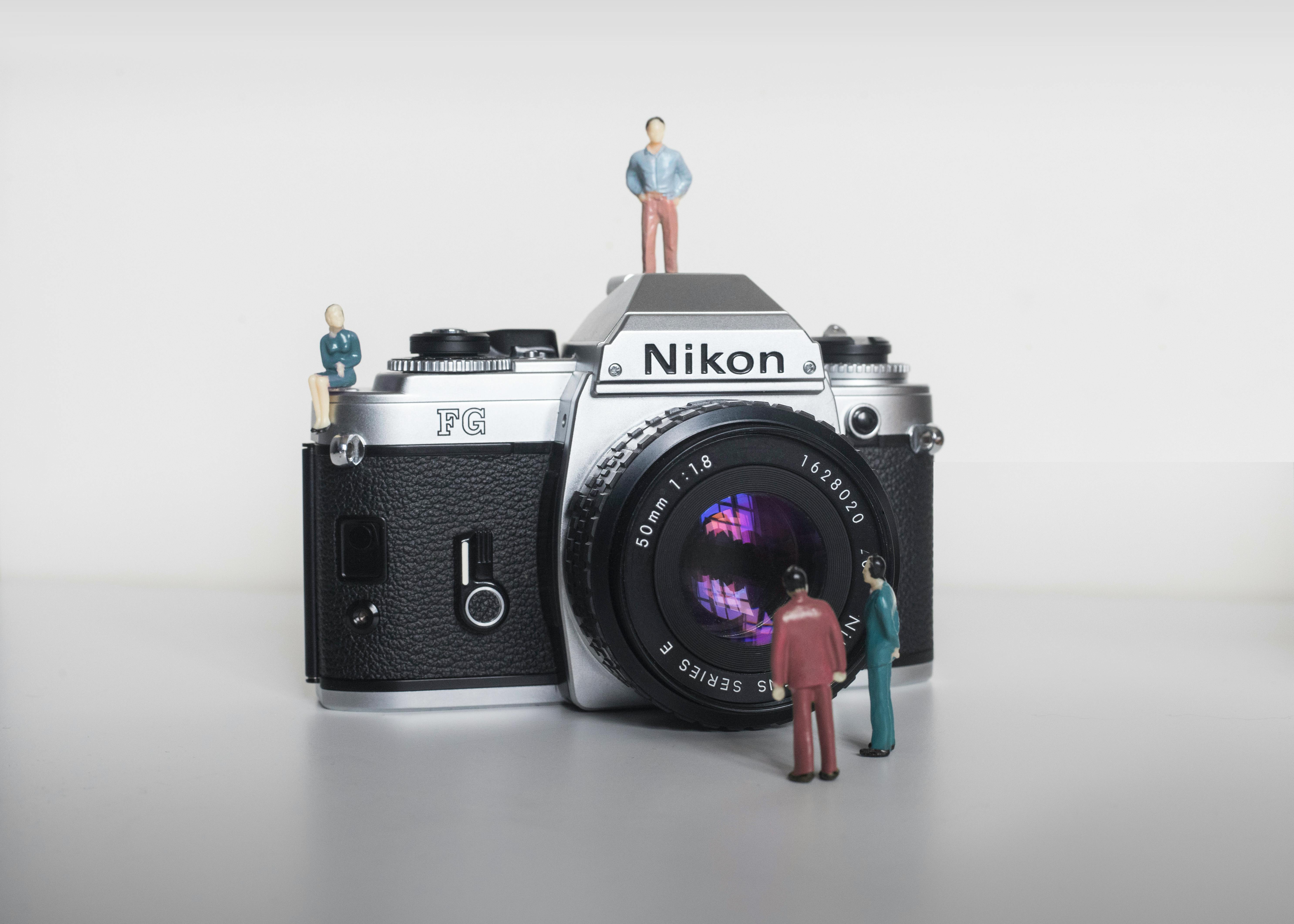 Creative shot of a vintage Nikon camera with miniature people figurines, emphasizing scale and artistry.