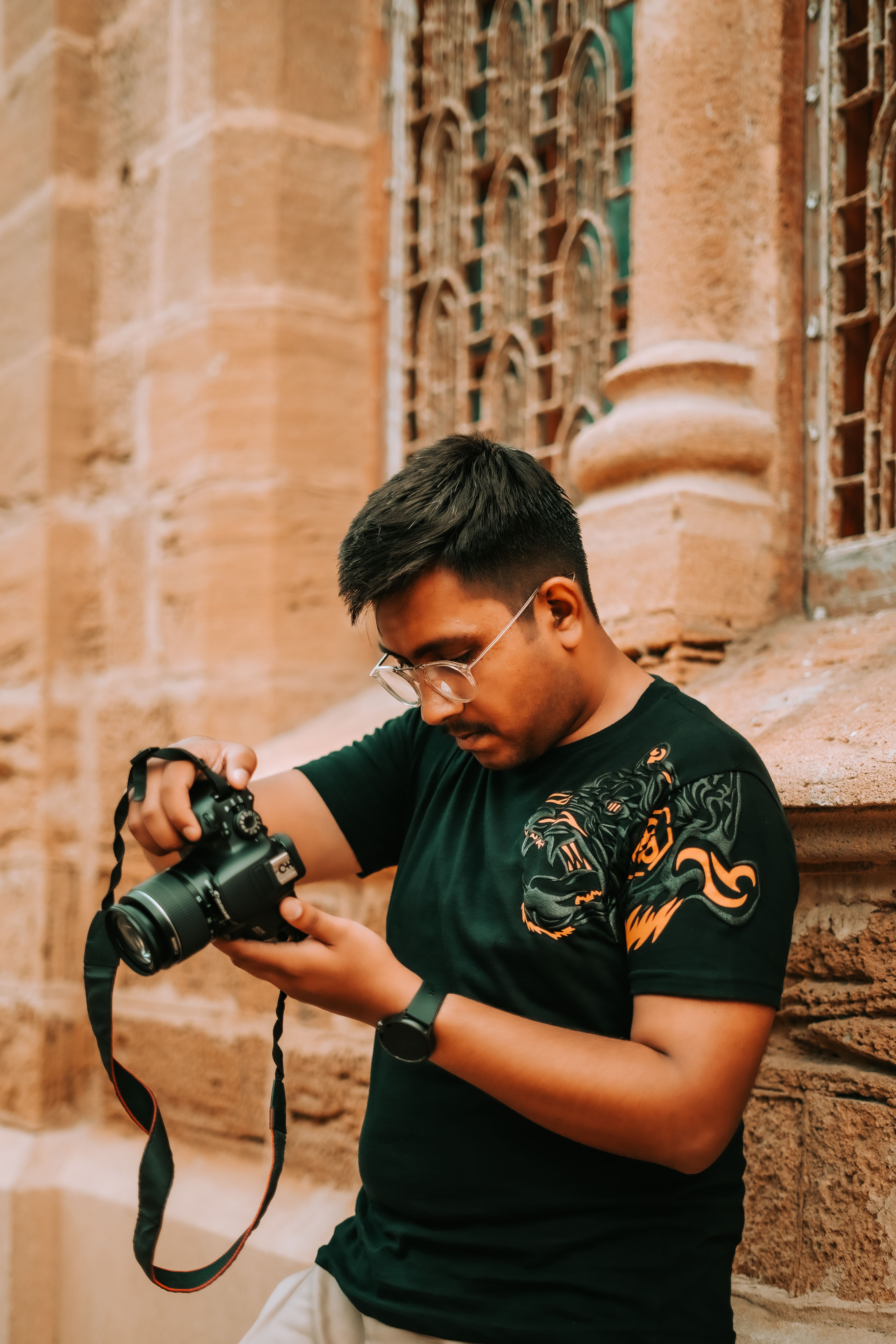 A young man with a camera examines his shots against an intricate architectural backdrop in Karachi, Pakistan.