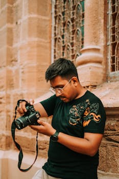 A young man with a camera examines his shots against an intricate architectural backdrop in Karachi, Pakistan.