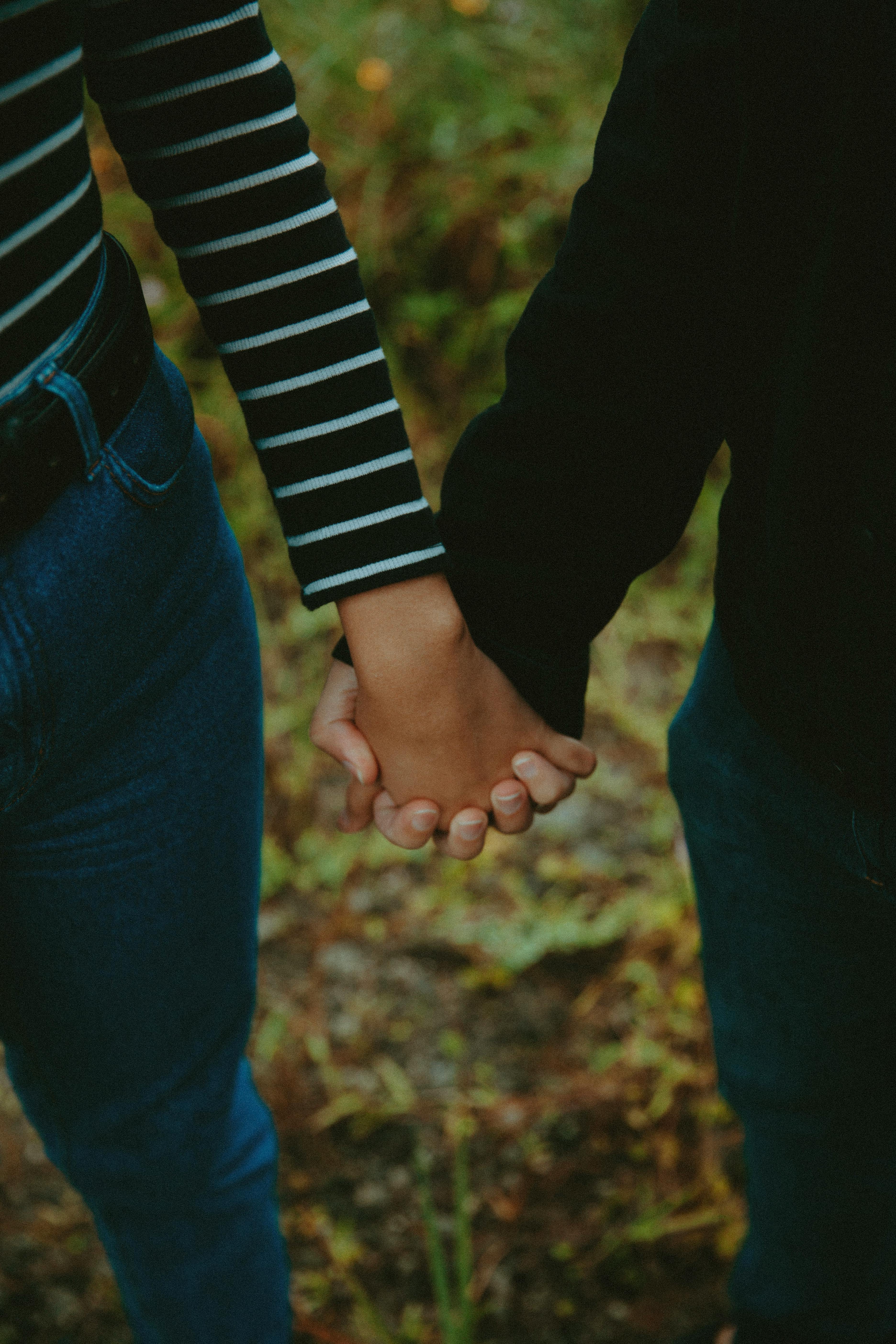 A couple holding hands outdoors, symbolizing love and connection, with a blurred natural background.