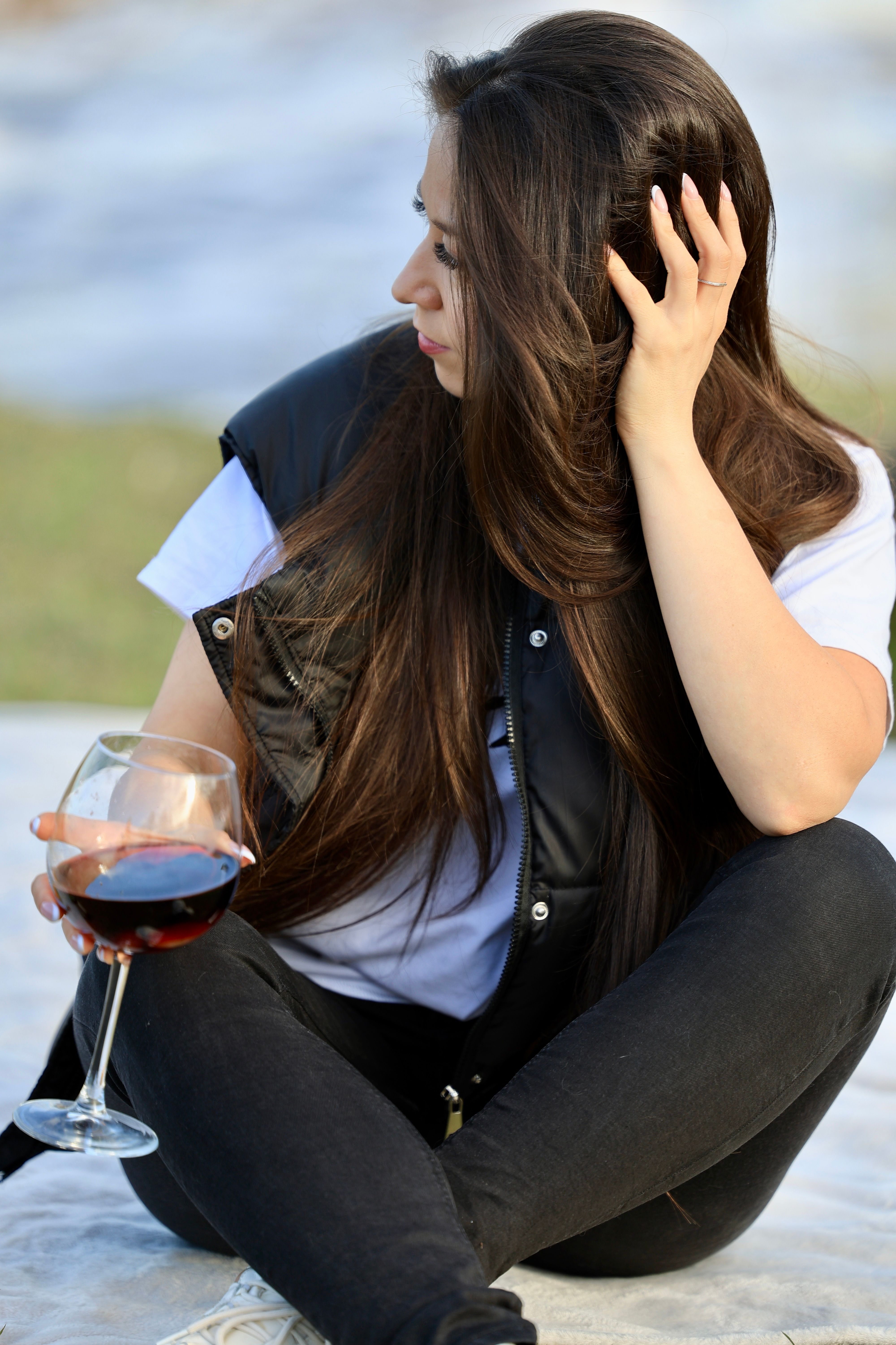 A woman sitting outdoors holding a glass of red wine, enjoying leisure time.