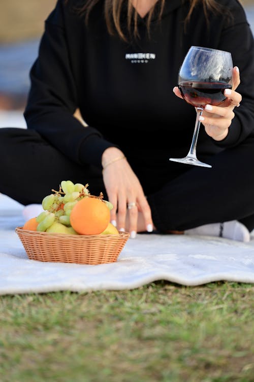 A woman holding a glass of wine and a basket of fruit