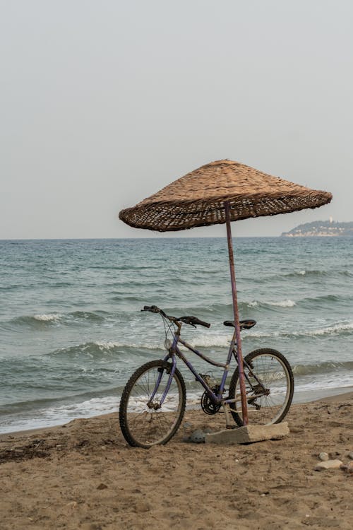 A bicycle is parked under an umbrella on the beach