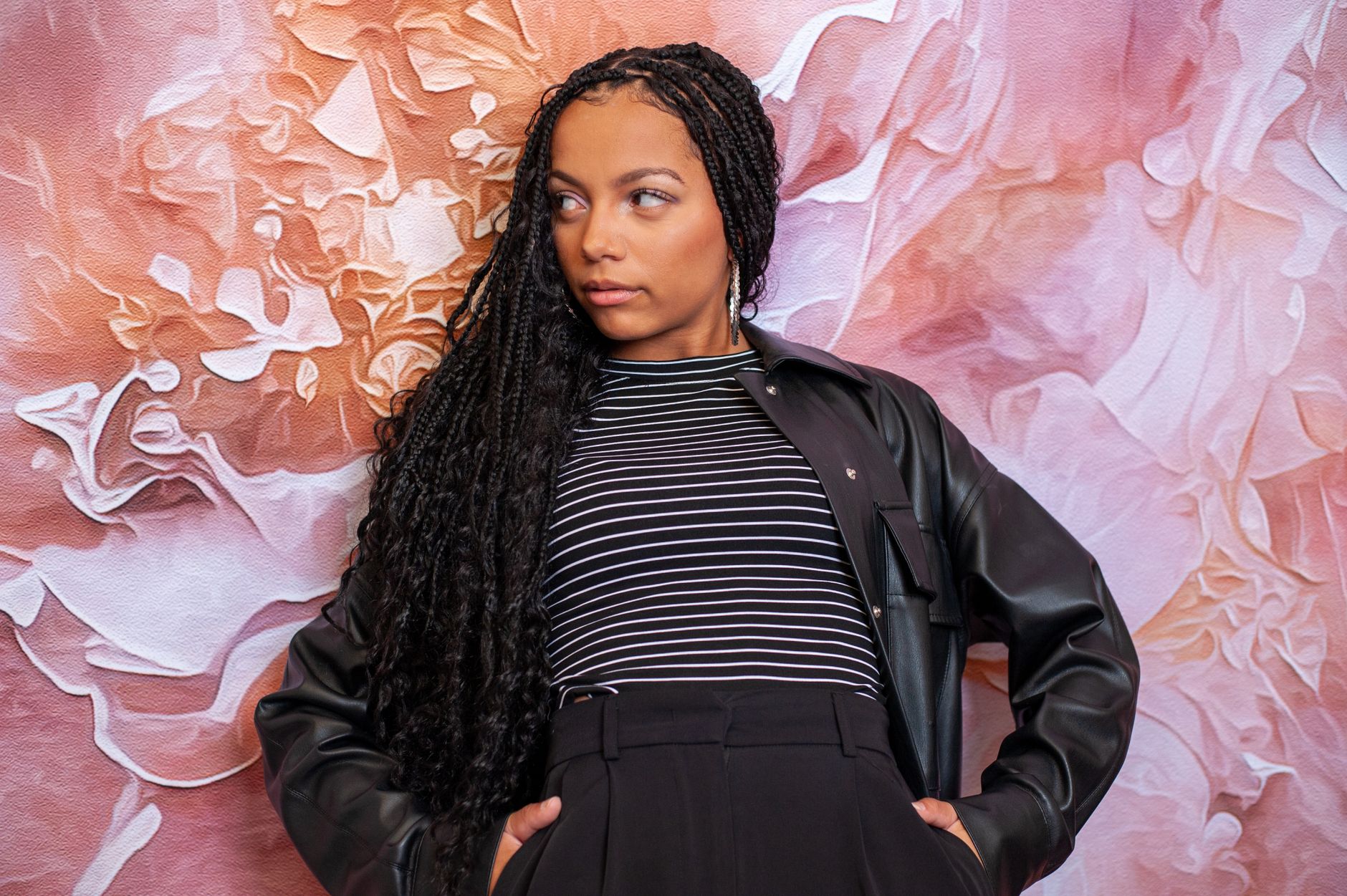 A woman with locs photographed against a painted wall.