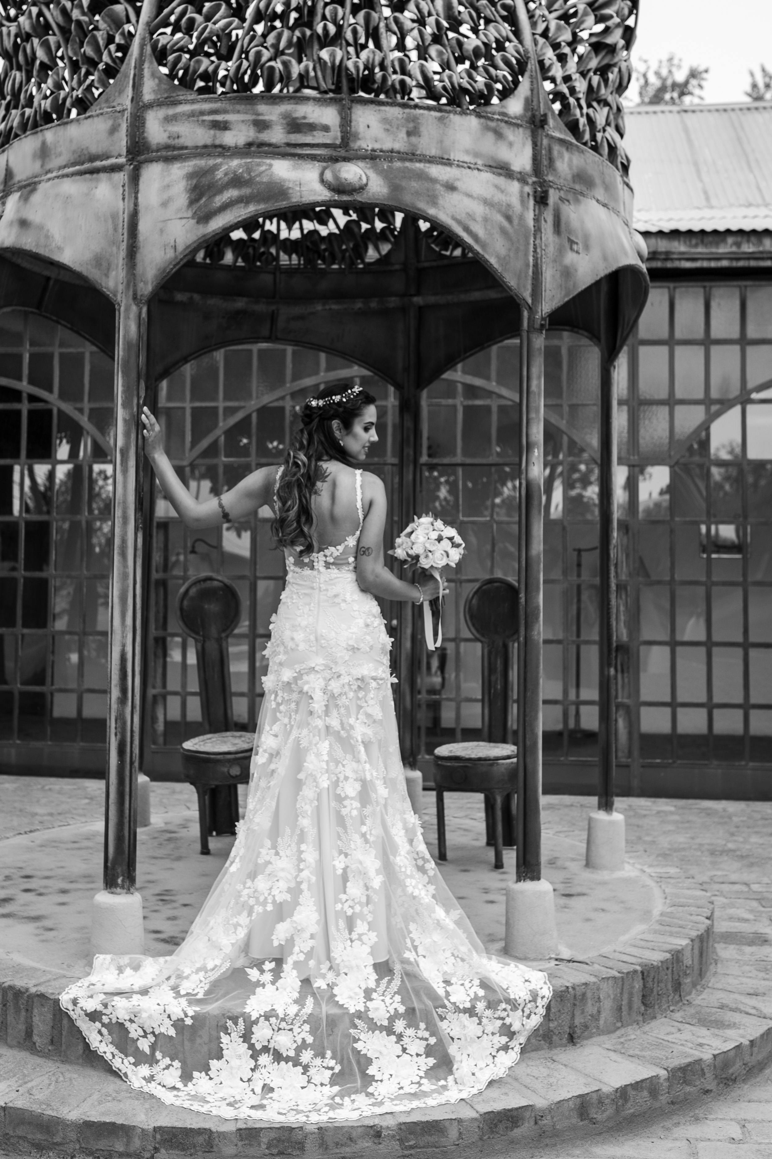 Black and white portrait of a bride standing in a gazebo holding flowers, showcasing elegance.