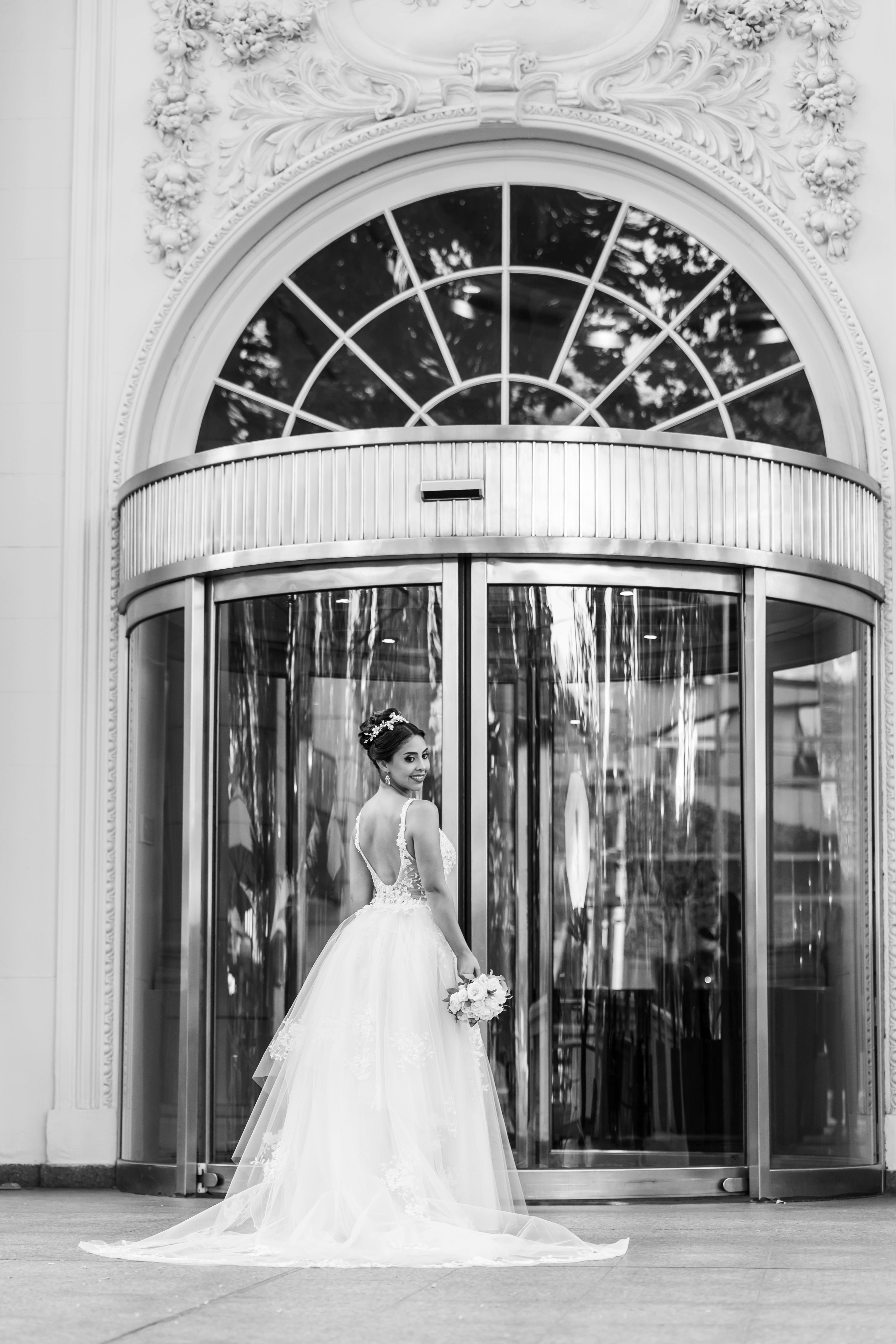 Charming bride in a wedding dress standing at an ornate entrance. Perfect for elegance and urban wedding themes.