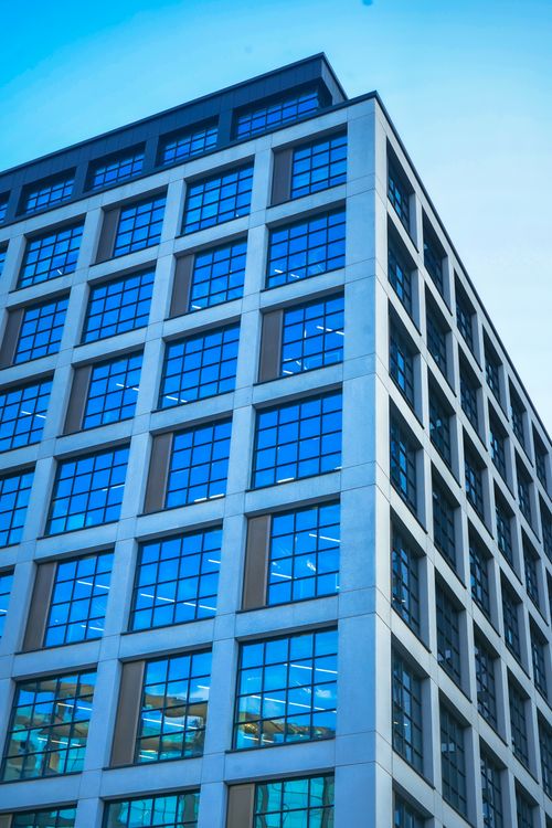 Free A sleek, modern office building with a reflective glass facade against a blue sky. Stock Photo
