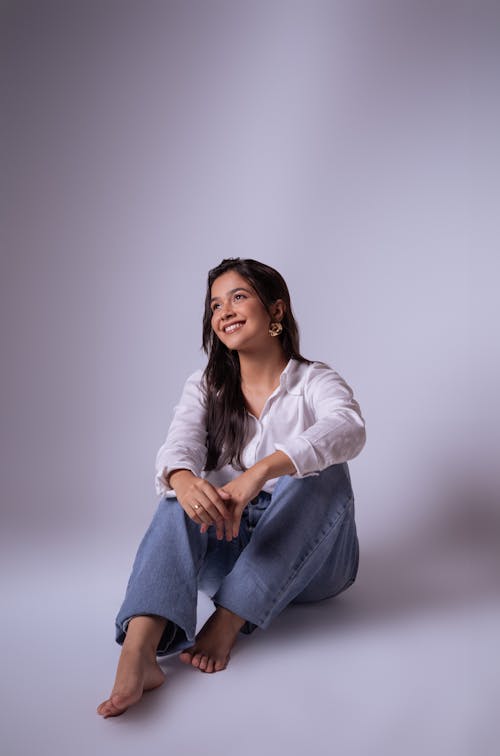 Free Woman in White Shirt and Jeans Sitting on Floor in Studio Stock Photo