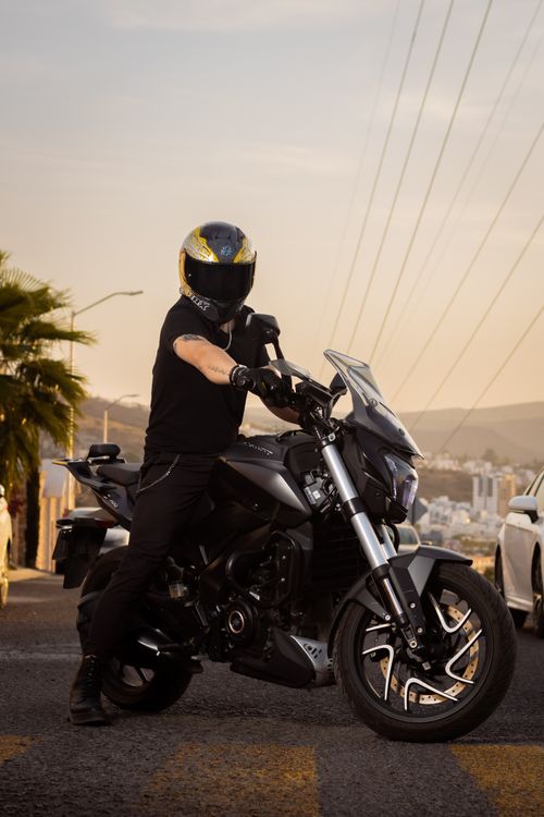 Free Man on a black motorcycle wearing a helmet on city streets at sunset. Stock Photo