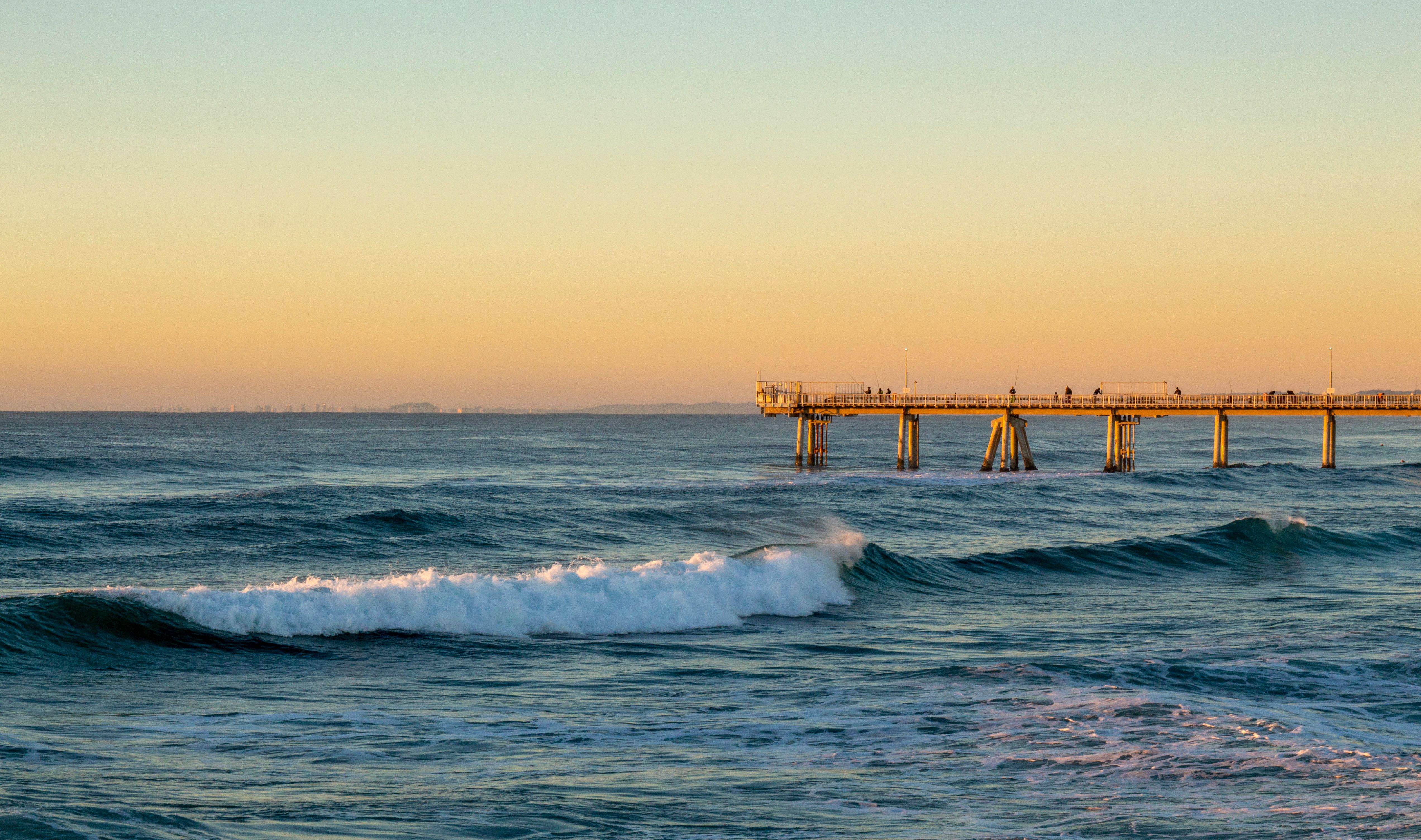 Captivating sunset at Gold Coast's pier with waves crashing beneath a golden sky. - Gold Coast